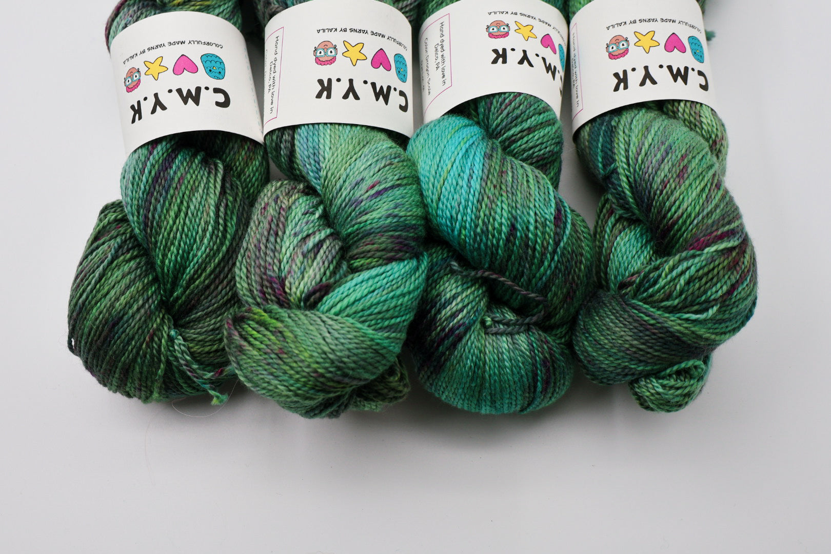 Four skeins of green yarn with colorful labels on a white background