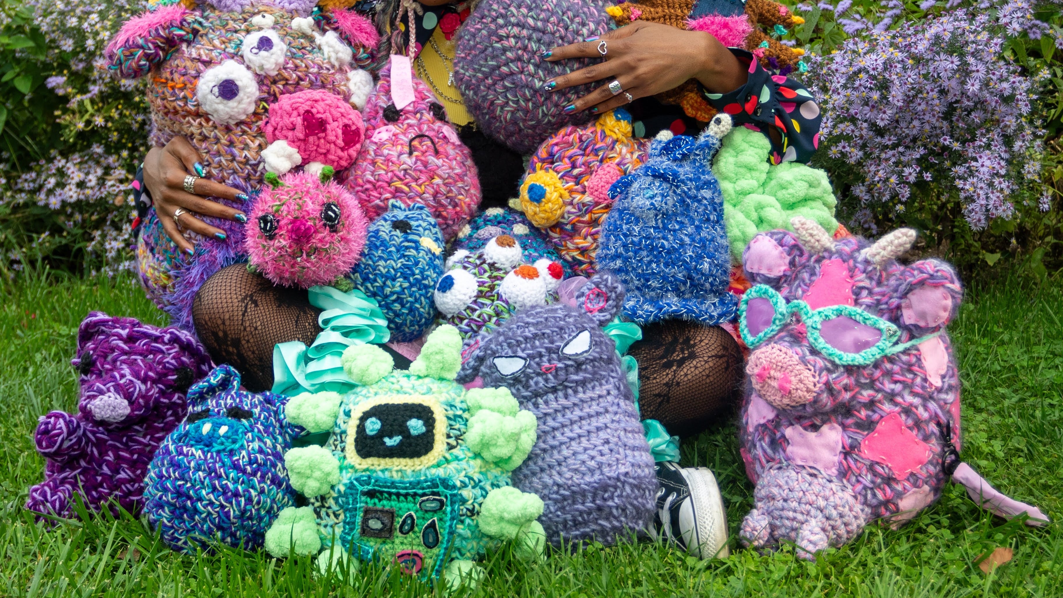 Person surrounded by colorful crocheted toys in a garden setting